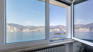 A room with a large window overlooking a mountainous landscape and a body of water. - Lake View Casa di Sandra Apartment with Lake View, Wi-Fi, and Air Conditioning (Malcesine)