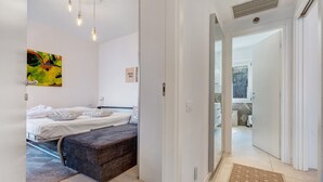 A bedroom with two beds, a bench, a colorful abstract painting, and a view to a balcony. - Lake View Casa di Sandra Apartment with Lake View, Wi-Fi, and Air Conditioning (Malcesine)