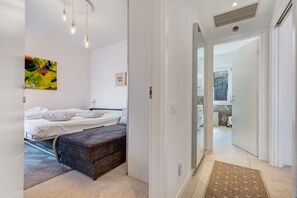 Une chambre avec deux lits, un banc, un tableau abstrait aux couleurs vives et une vue sur un balcon.