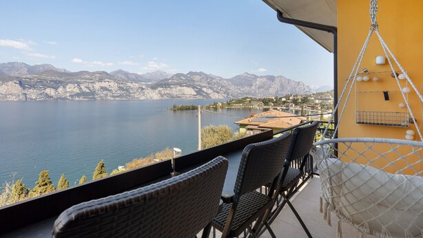 A balcony with wicker chairs and a hammock overlooking a lake with mountains in the background. - Lake View Casa di Sandra Apartment with Lake View, Wi-Fi, and Air Conditioning (Malcesine)