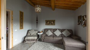 Uma sala de estar com sofá, tapete estampado, luminária pendente e relógio de parede.
