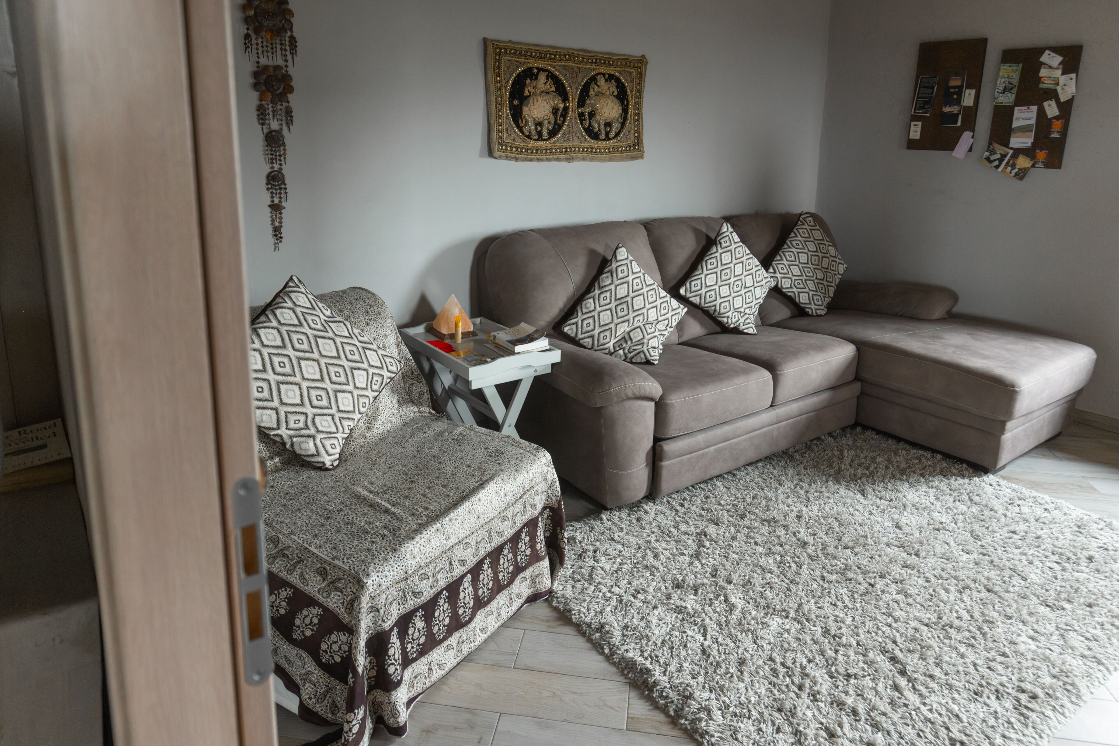 A living room with a sectional sofa, patterned cushions, a small side table, and a decorative wall hanging.