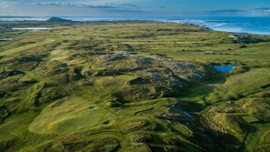 Eine Vogelperspektive eines Golfplatzes mit welligem Gelände und Wasserflächen.