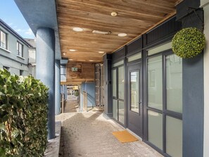 A covered walkway with a wooden ceiling, glass doors, and a small garden area. - Village Centre Haven (Clifden)
