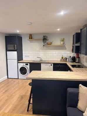 A compact kitchen with built-in appliances, a wooden countertop, and a dark-colored sofa. - Village Centre Haven One Bed Apartment (Clifden)