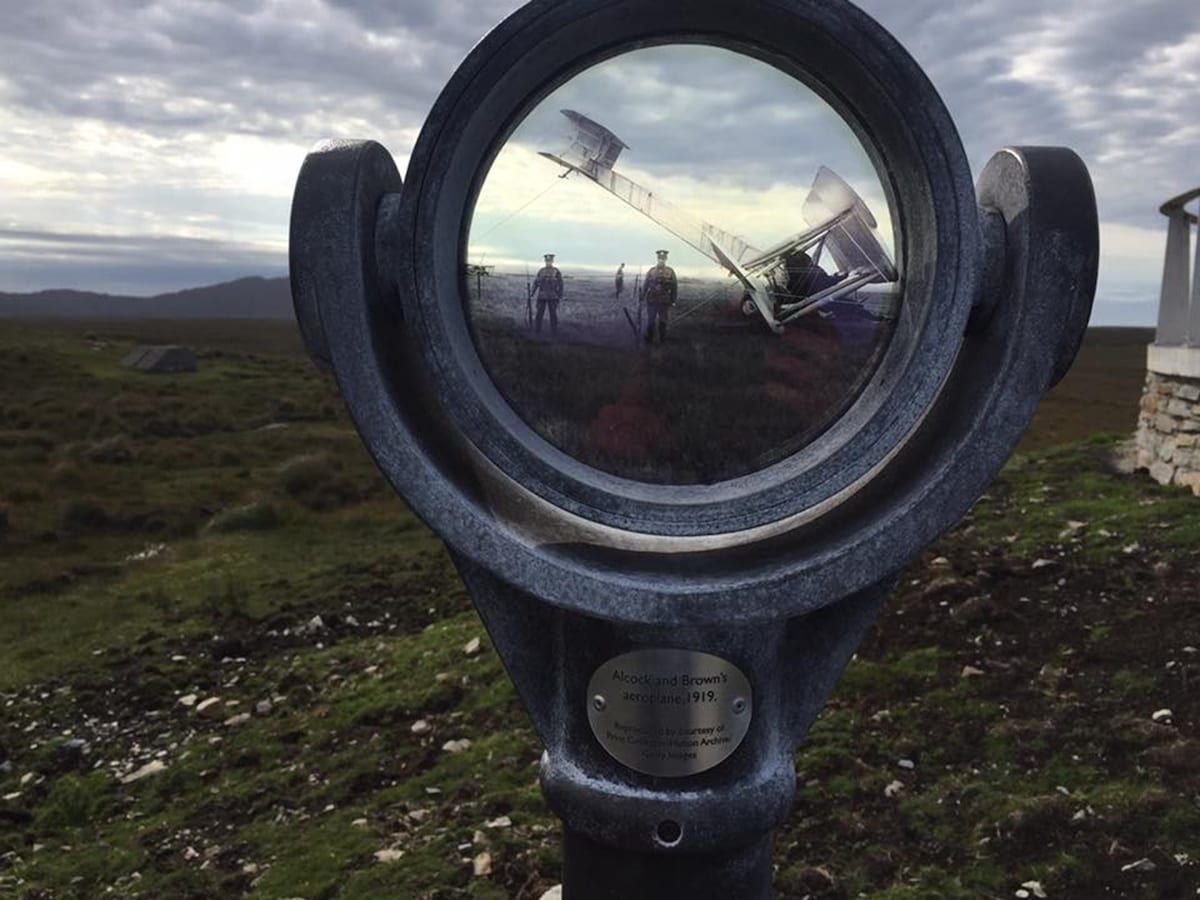 A circular viewing device with a plaque, set against a landscape with a cloudy sky.