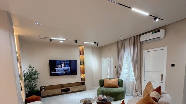 A modern living room with a large sectional sofa, a flat-screen TV, a coffee table, and a potted plant. - L Rina Apartment (Lekki)
