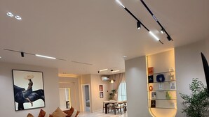 A modern living room with a sectional sofa, a green ottoman, and a dining area in the background. - L Rina Apartment (Lekki)