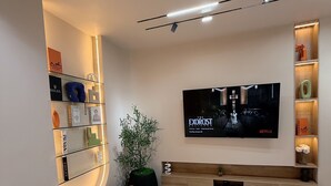 A modern living room with a flat-screen TV, a curved shelving unit, a potted plant, and a bench. - L Rina Apartment (Lekki)