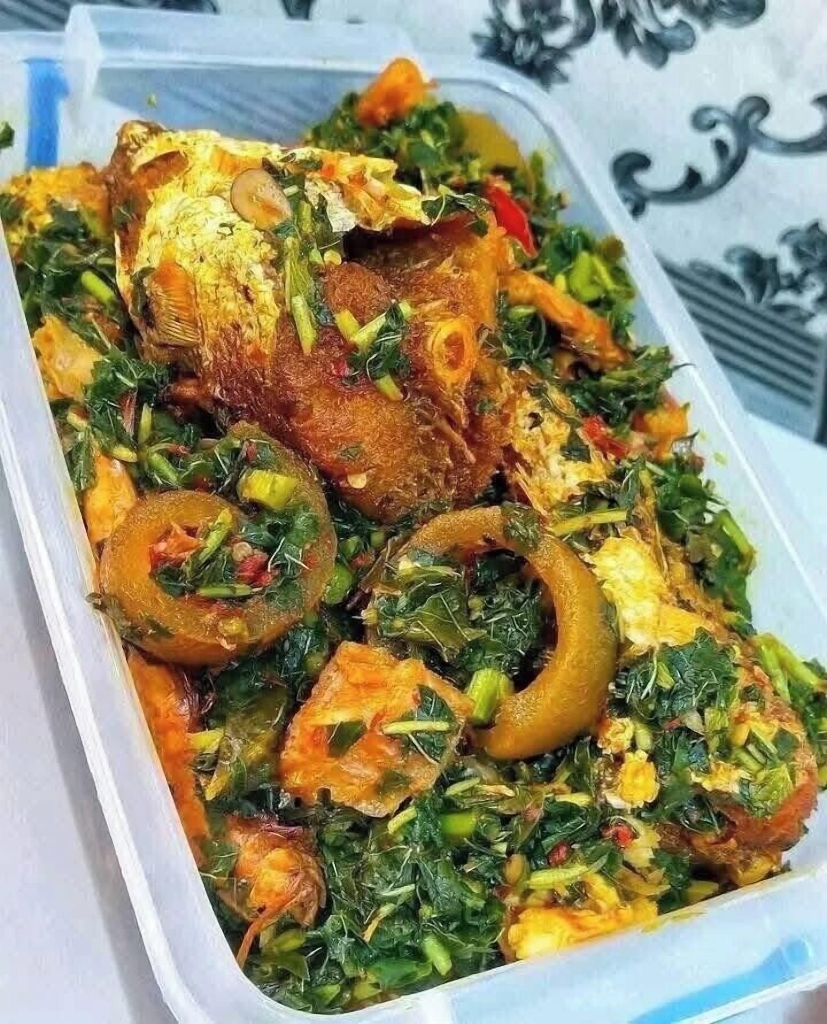 A meal with fish, greens, and slices of tomato in a container.