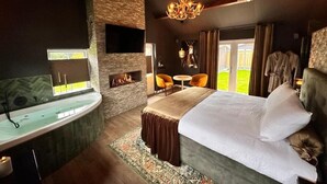 A bedroom with a large bed, a sitting area with chairs, a fireplace, and a view of the outdoors. - Wellness Tuin  Luxury Suites & Lodges (Horst)