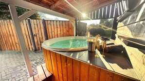 A hot tub with a wooden deck, a metal bucket, and a towel. - Wellness Tuin  Luxury Suites & Lodges (Horst)