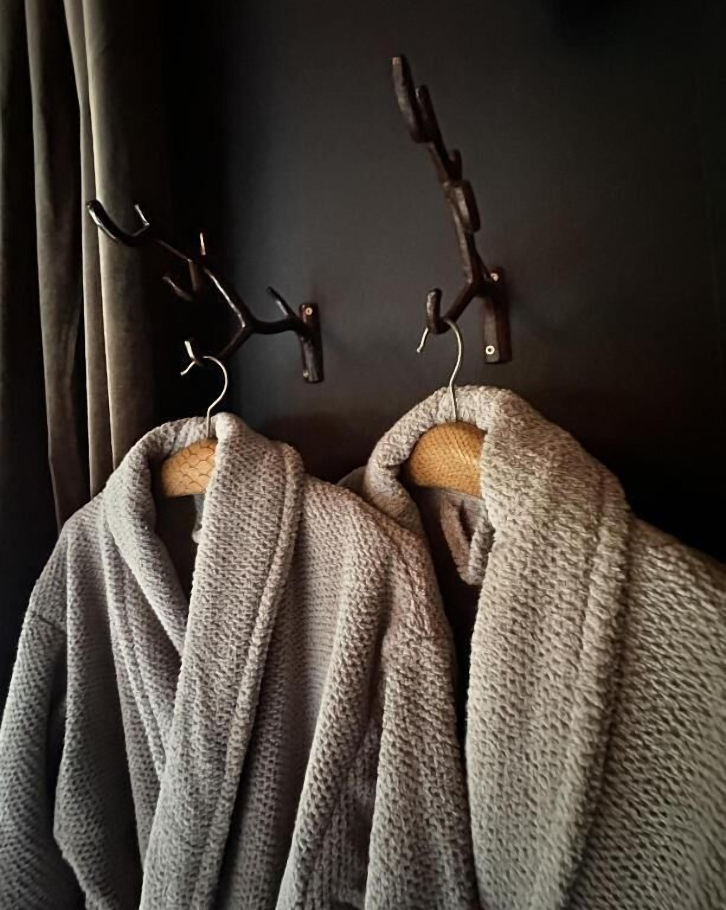 Two grey robes hanging on wooden hooks against a dark wall.