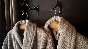 Two grey robes hanging on wooden hooks against a dark wall.