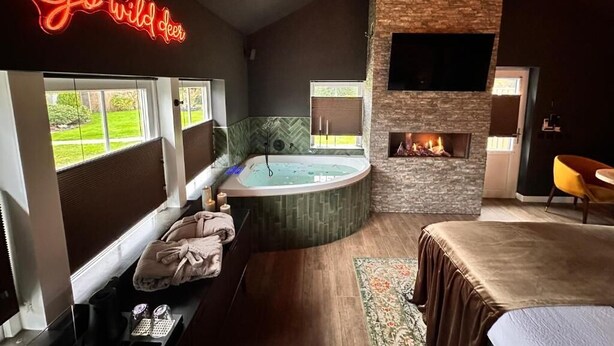 A room with a fireplace, a large window, a bathtub, and a neon sign. - Wellness Tuin  Luxury Suites & Lodges (Horst)