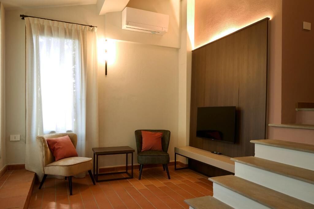 Ein Wohnzimmer mit einer Couch, zwei Sessel, einem kleinen Tisch, einem an der Wand montierten Fernseher und einer Treppe.