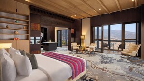 Una habitación de hotel amplia con una cama grande, varias zonas de estar y vistas a la montaña.
