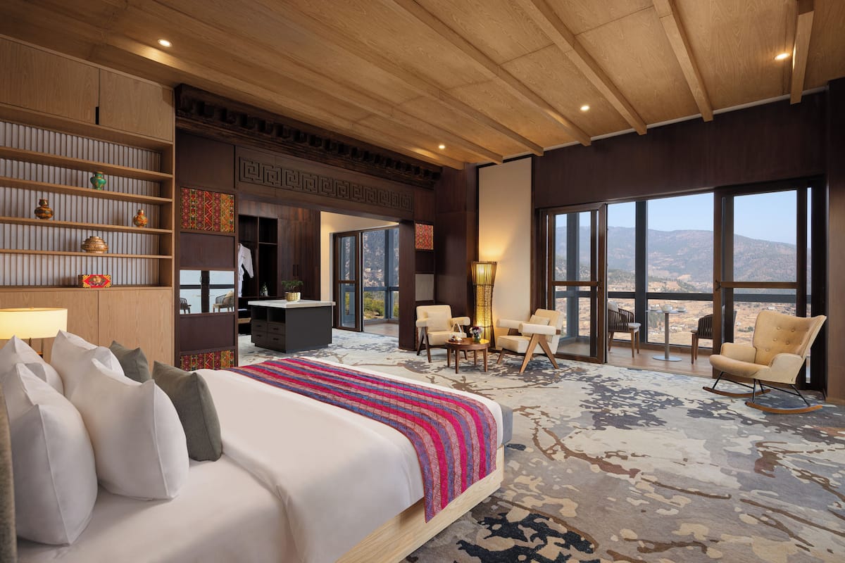A spacious hotel room with a large bed, multiple seating areas, and a view of the mountains.