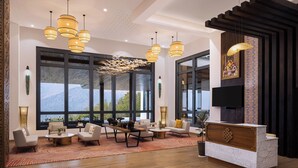 A modern hotel lobby with a reception desk, seating area, large windows, and pendant lighting. - Dawa At Hilltop By Heeton Paro Bhutan (Paro)