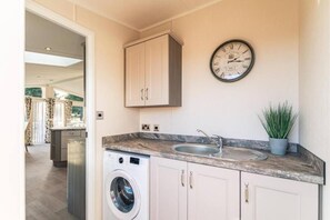 A kitchen with a washing machine, a sink, a clock, and a cabinet. - Host & Stay | Woodland Jewel Lodge (Pocklington)