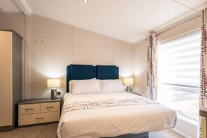 A hotel room with a bed, two bedside lamps, a nightstand, a wardrobe, and a window with curtains. - Host & Stay | Woodland Jewel Lodge (Pocklington)
