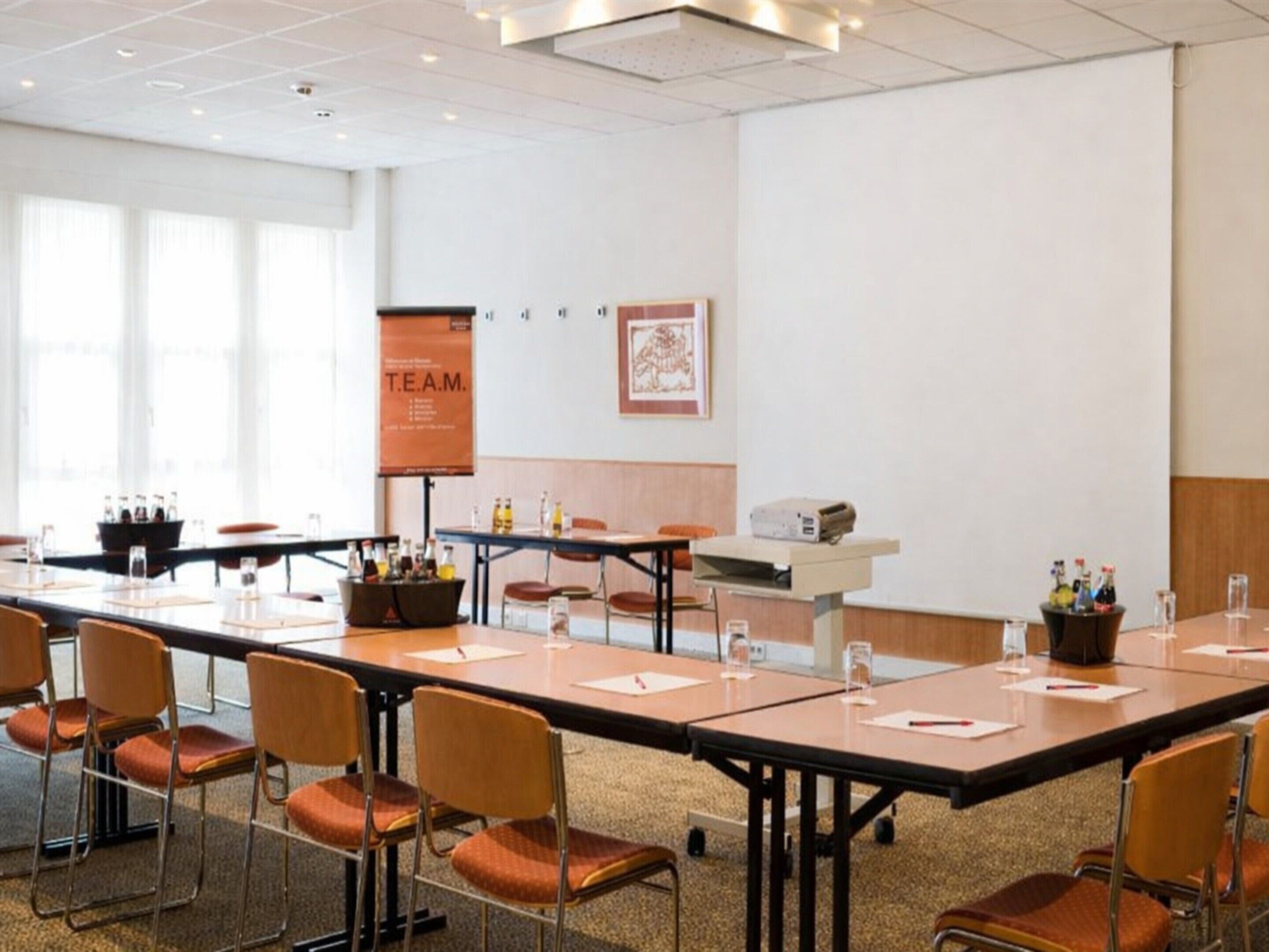 A conference room with long tables, chairs, a projector, and a banner on the wall.
