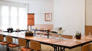 A conference room with long tables, chairs, a projector, and a banner on the wall.