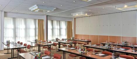 A conference room with multiple tables, chairs, and a large whiteboard wall.