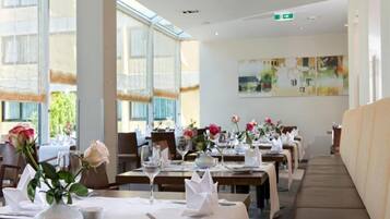 Een restaurant met gedekte tafels, grote ramen en een schilderij aan de muur.
