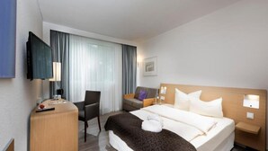 A hotel room with a bed, a desk, a chair, a TV, and a window with curtains. - Sunday Saarbruecken Sued Deluxe Double Room (Saarbrücken)