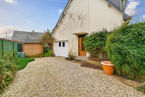 Ein Haus mit Kopfsteinpflasterauffahrt, einer Holztür und einem großen Kübelpflanzen.