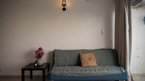 Une pièce avec un canapé bleu, une petite table sur laquelle est posé un vase de fleurs et un luminaire fixé au mur.