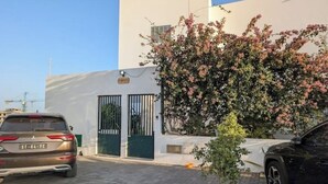 Un espace de stationnement avec deux voitures, un bâtiment à la façade blanche et un arbre en fleurs.