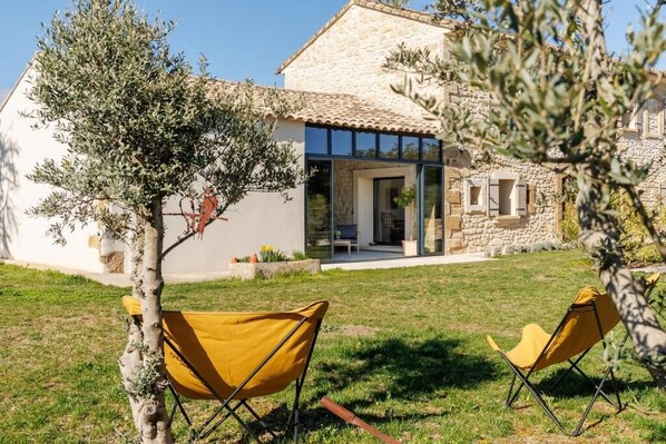 A stone building with a glass door entrance, a small patio, and two yellow chairs. - Mas le Jas (Cavaillon)