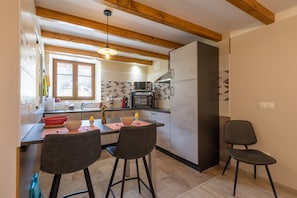 A kitchen with wooden beams, a window, a microwave, and two bar stools. - Gîte "Gîte Des Roches" with Private Terrace, Private Garden, and Wi-Fi (Le Clerjus)