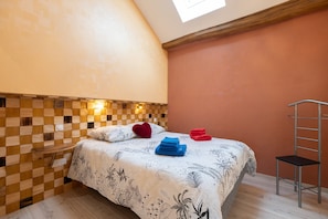 A bedroom with a checkered wall, a bed with a floral bedspread, a red heart pillow, and a metal chair. - Gîte "Gîte Des Roches" with Private Terrace, Private Garden, and Wi-Fi (Le Clerjus)