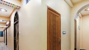 A hallway with a wooden door, a refrigerator, and a light switch on the wall. - Hotel Singh Palace (Purnia)