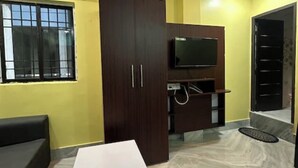 A room with a TV on a wooden cabinet, a white table, a sofa, and a patterned floor. - Hotel Singh Palace (Purnia)