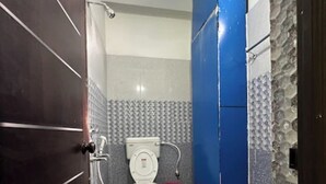 A bathroom with a toilet, a pink bucket, and a marble floor. - Hotel Singh Palace (Purnia)