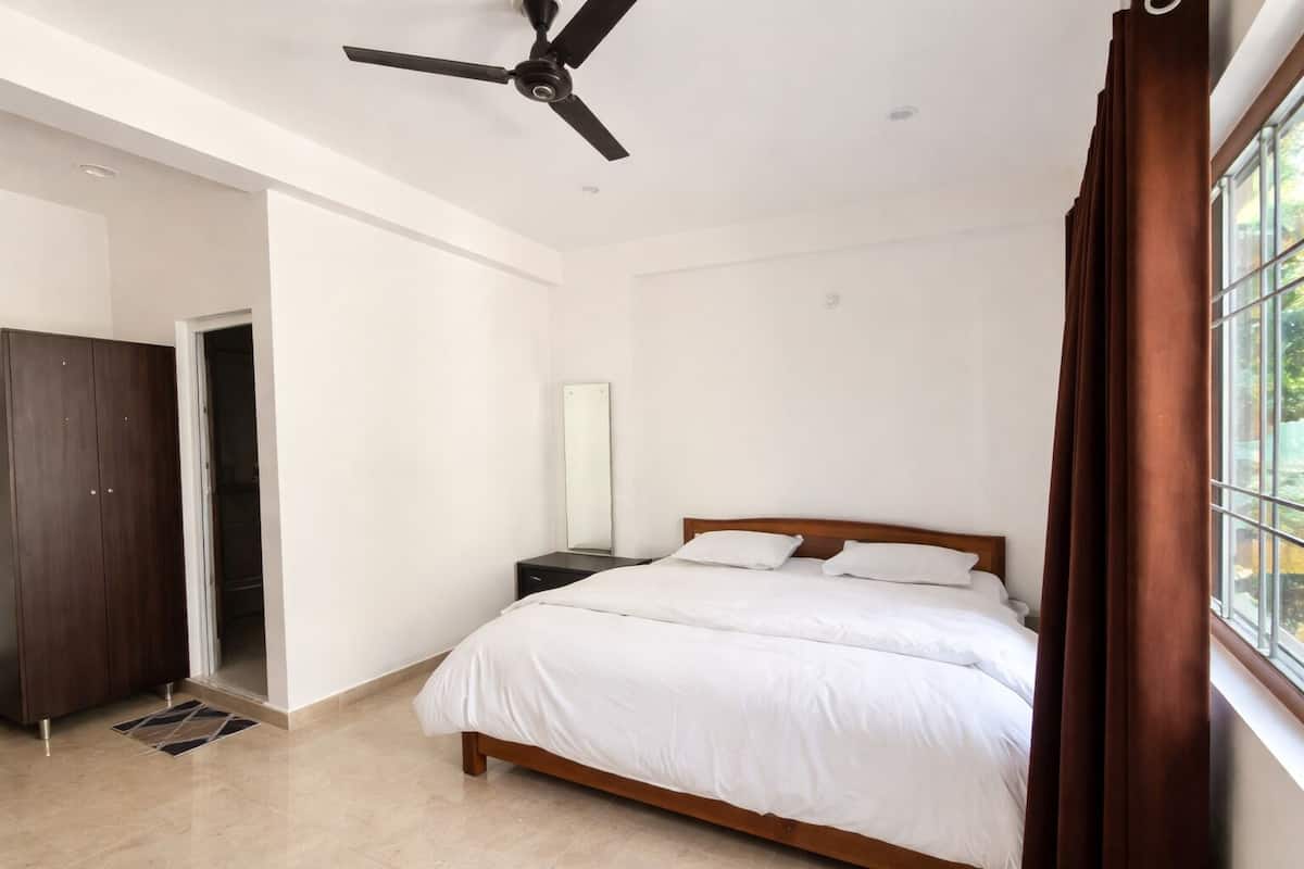 A bedroom with a bed, a ceiling fan, a nightstand, a mirror, and a window with curtains.