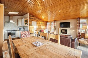 A cozy cabin interior with a wooden dining table, chairs, a kitchen area, and a fireplace. - Host & Stay | GRE08 Crystal Lodge (Amotherby)