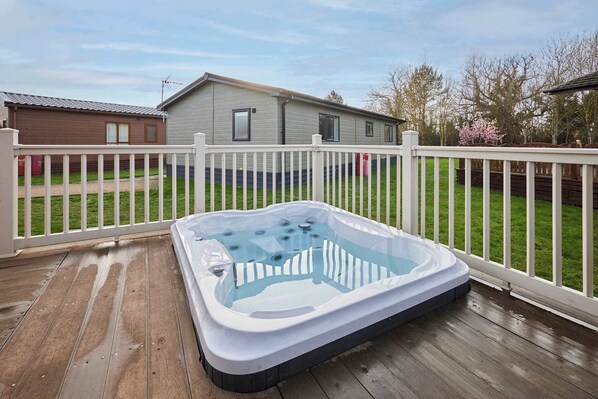 Ein Whirlpool auf einer Holzterrasse mit einem weißen Zaun, ein Haus im Hintergrund und eine Rasenfläche.