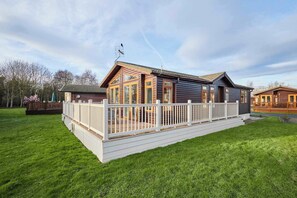 Eine Holzhütte mit einer Terrasse, großen Fenstern und einer sichtbaren Satellitenschüssel.