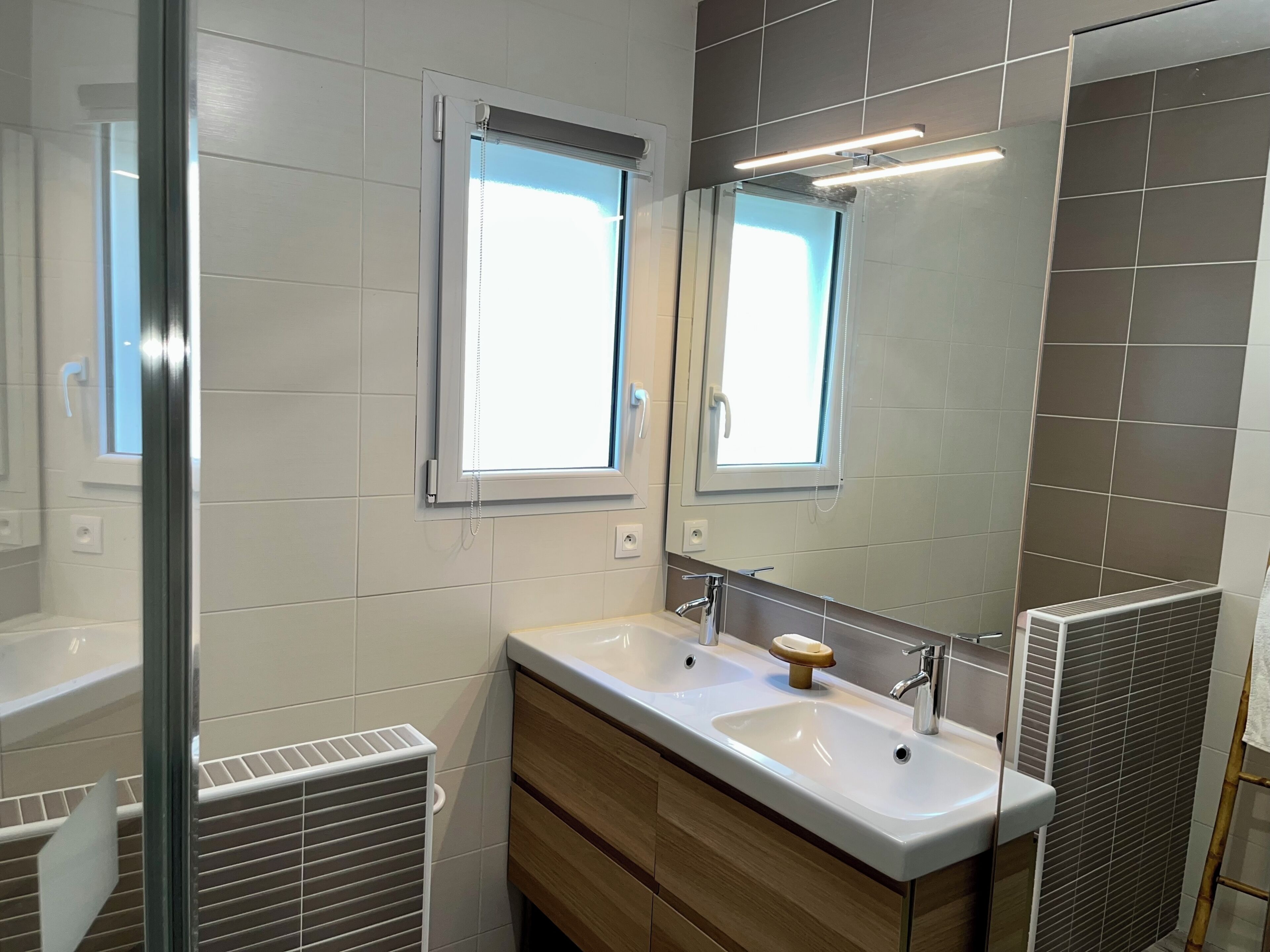 A modern bathroom with two sinks, a mirror, and a window.