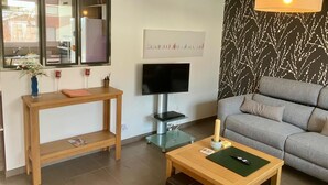 Ein modernes Wohnzimmer mit grauem Sofa, einem Holztisch, einem Fernseher und einer Wandlampe.