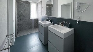 Une salle de bain moderne avec deux lavabos, une douche et un sèche-cheveux fixé au mur.