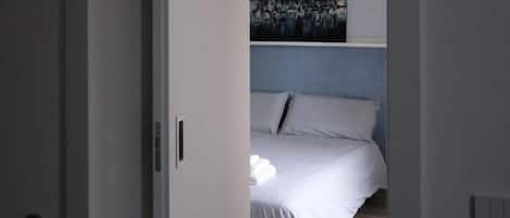 A bedroom with a bed, a painting on the wall, and a door.