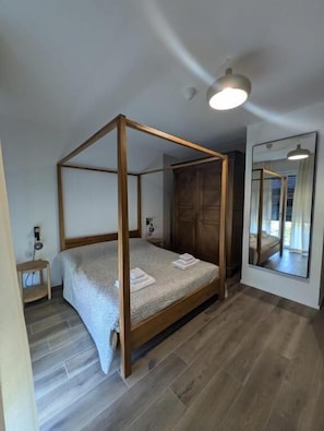 A four-poster bed with a wooden frame, a bedside table, a large mirror, and a wooden wardrobe. - B&b Colori del lago (Brebbia)