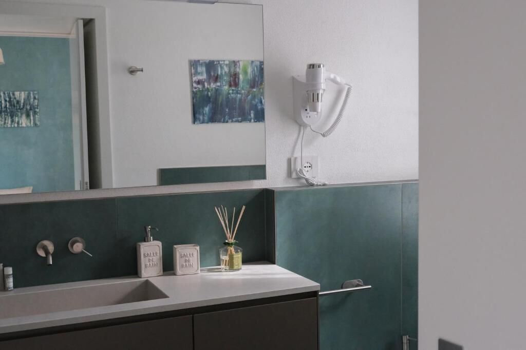 A bathroom with a mirror, a sink, a hairdryer, and a bottle of reed diffuser.