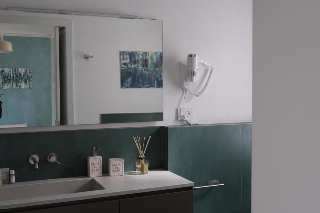Une salle de bain équipée d’un miroir, d’un sèche-cheveux, d’un flacon de savon liquide et d’un petit panneau encadré.